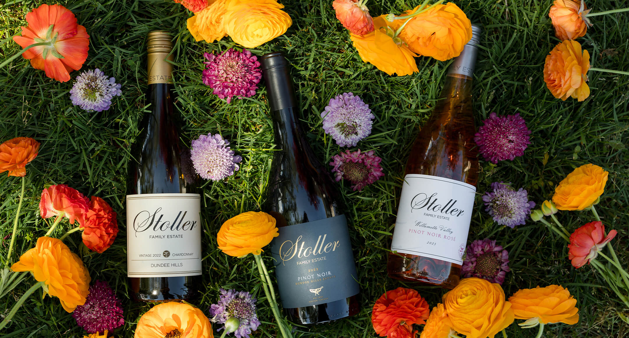 three bottles of Stoller wine layed out on grass and surrounded by colorful flowers